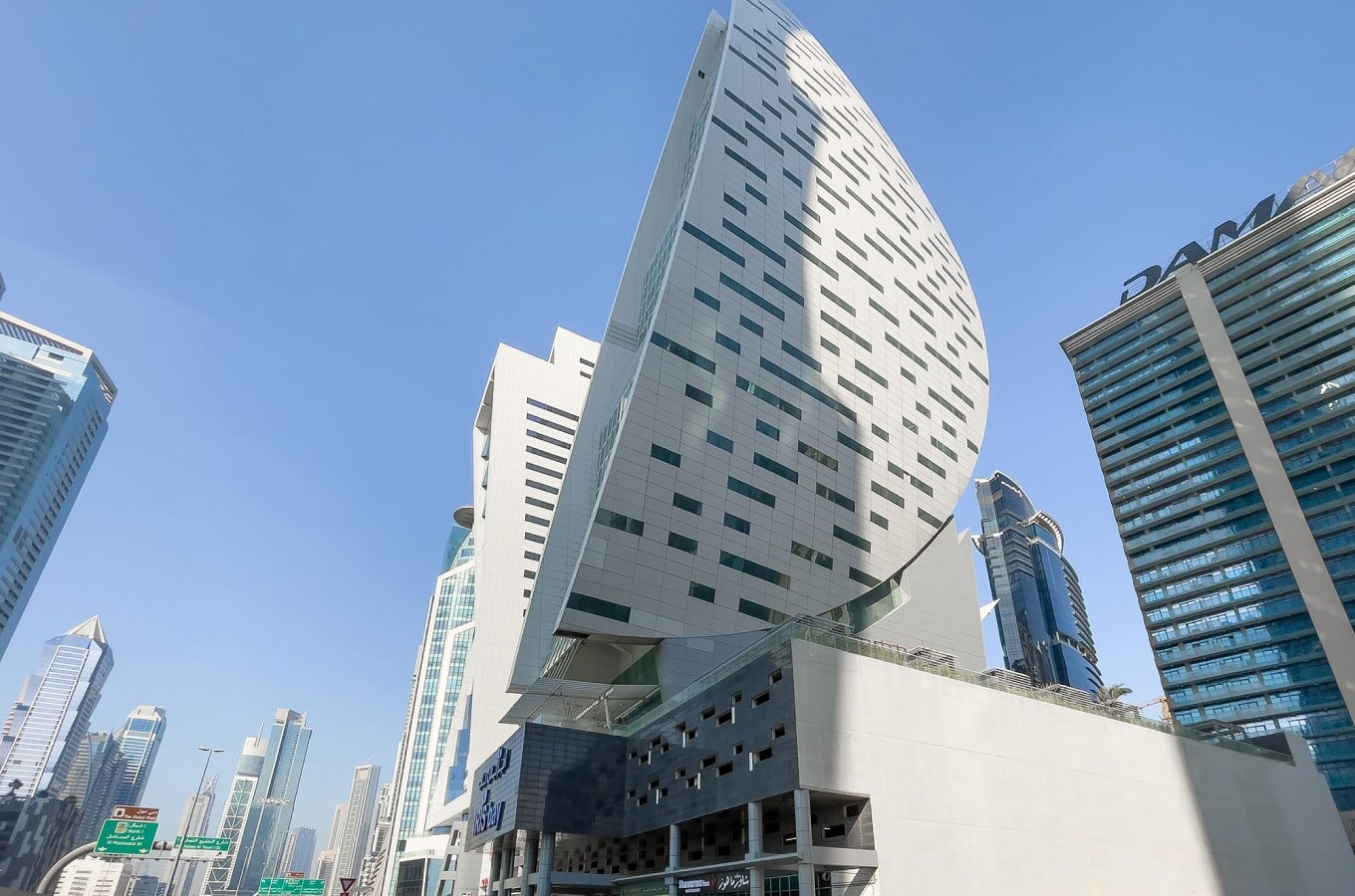 Leaf-shaped tower among high-rises seen from below under a blue sky