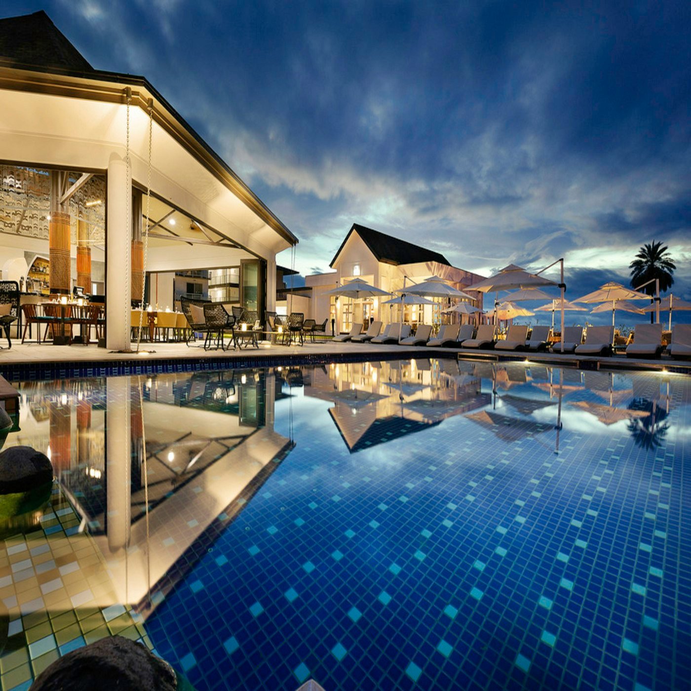 Resort-style pool at dusk with a lit pavilion and parasols