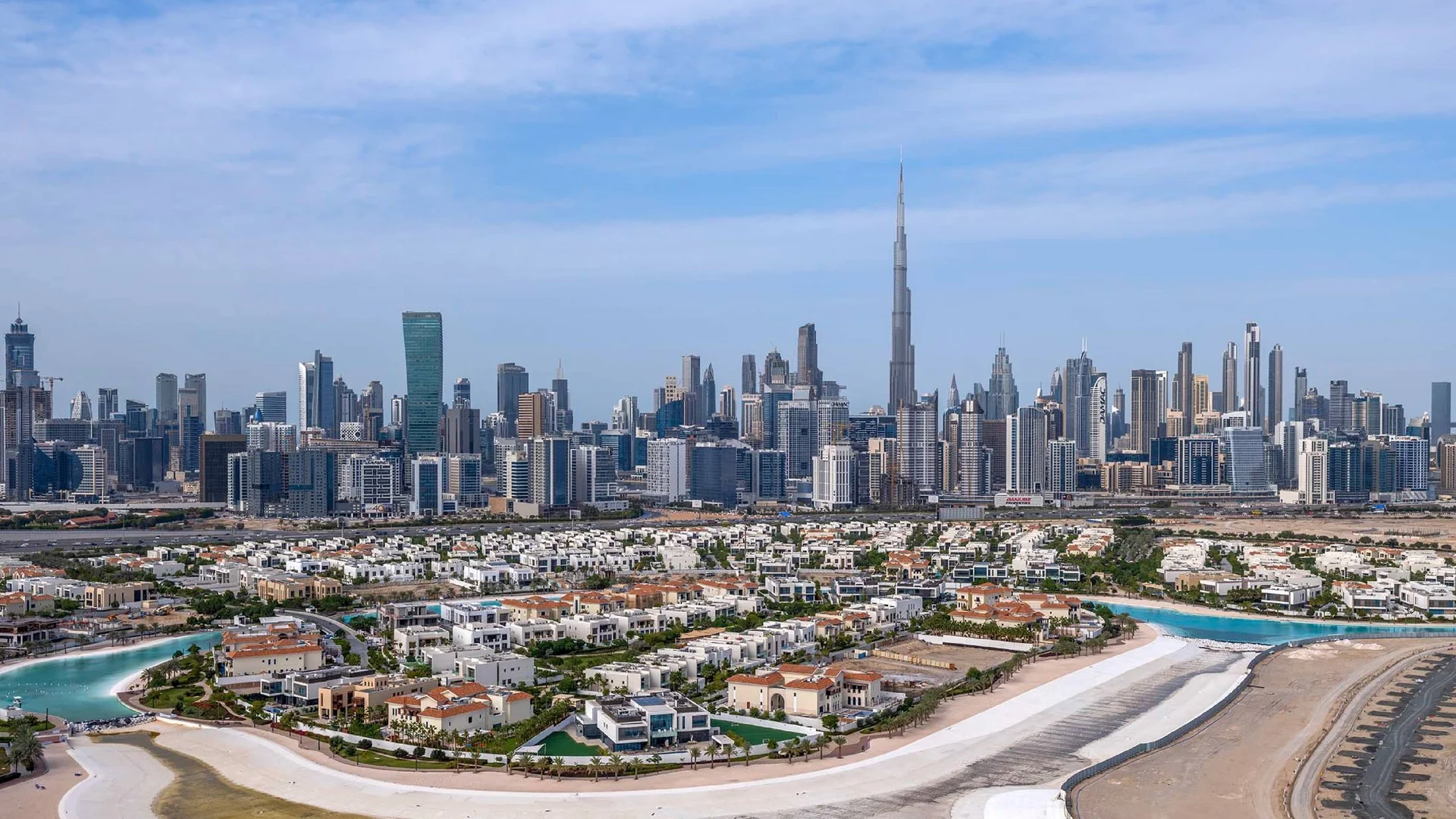 Aerial view of a villa district with a lagoon beach and the Dubai skyline with Burj Khalifa behind