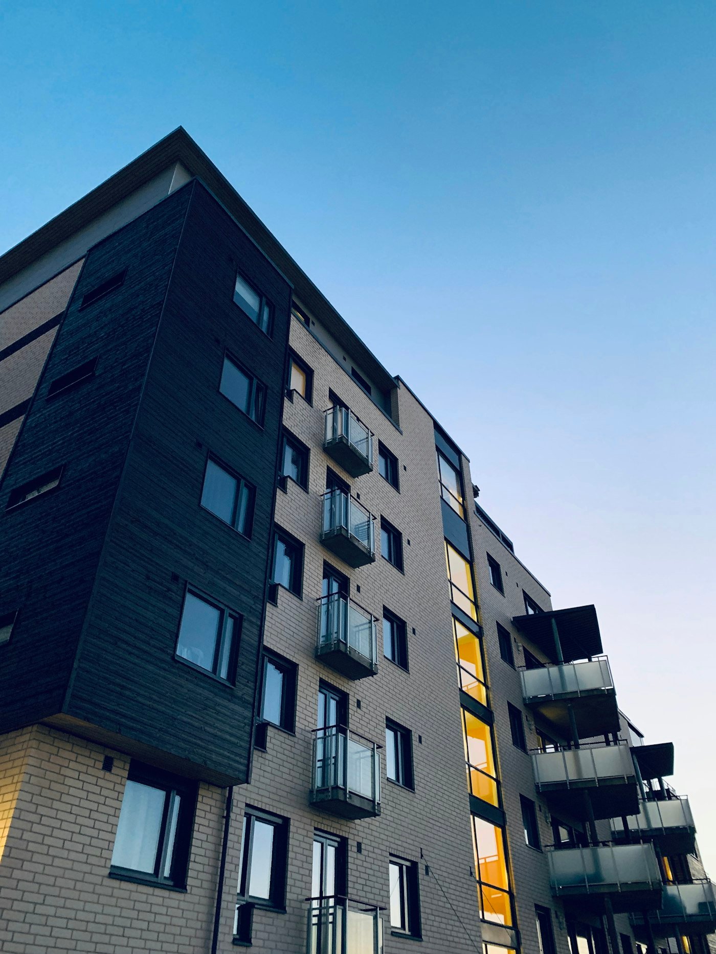 Dark-clad apartment building with balconies seen from below against a blue sky